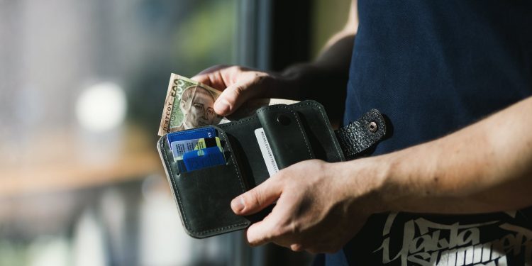 photograph of person holding black leather wallet with money